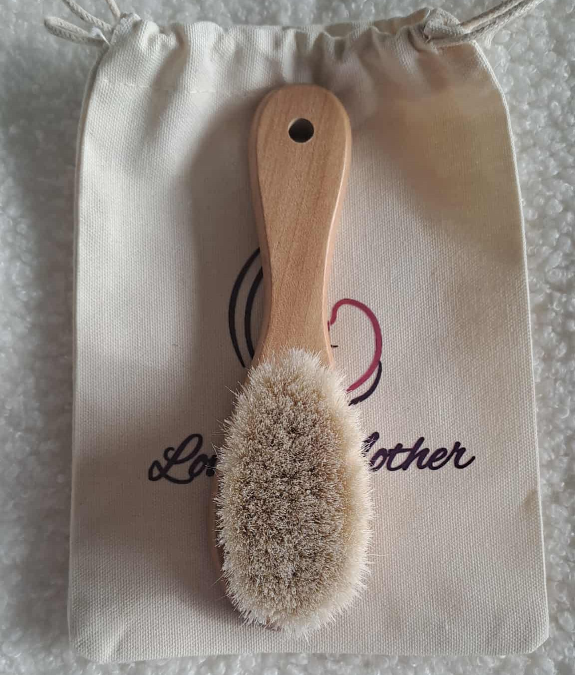 Wooden brush with natural bristles on a branded drawstring bag.