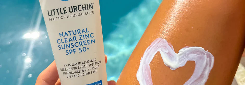 Little Urchin natural clear zinc sunscreen with a heart-shaped application on skin by a pool.