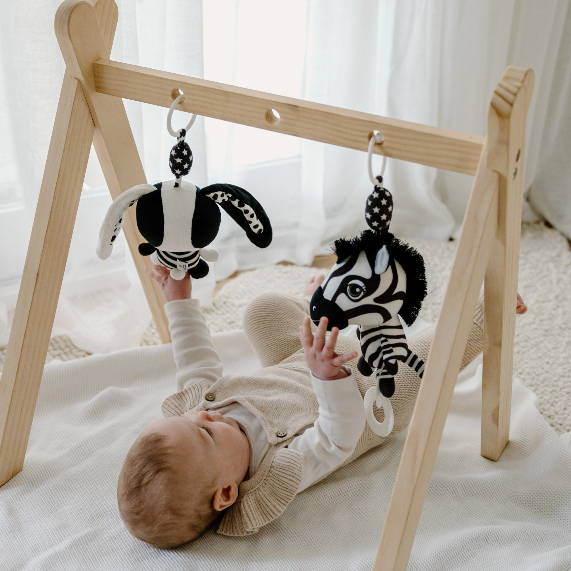 Baby playing with zebra toys on a wooden baby gym